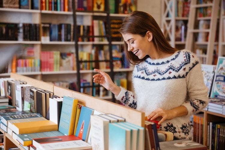 una mujer joven sonriendo escoge un libro en la librería