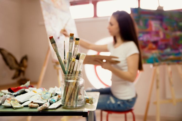 Mujer joven pintando sobre un lienzo en su estudio.